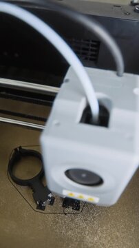 Vertical shot of 3D printer extruding black plastic filament to create robot components on print bed. Footage is ideal for technology, engineering, and rapid prototyping commercial projects