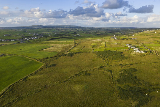 Aerial view of the lush green fields and rolling landscape of the Irish countryside under a cloudy sky in Doolin, County Clare, Ireland.