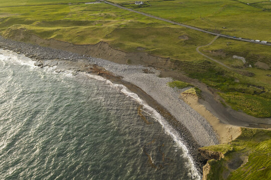 Aerial view of the rugged coastline with a pebble beach, grassy cliffs, and a coastal road in Doolin, County Clare, Ireland.