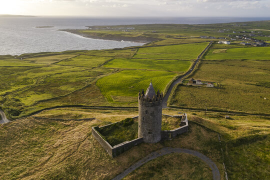 Aerial view of Doonagore Castle surrounded by lush green fields, stone walls, and the rugged coastline of the Atlantic Ocean in Doolin, County Clare, Ireland.