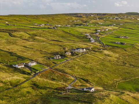 Aerial view of the rolling green hills and stone walls of the Irish countryside with scattered houses along a winding road in Doolin, County Clare, Ireland.