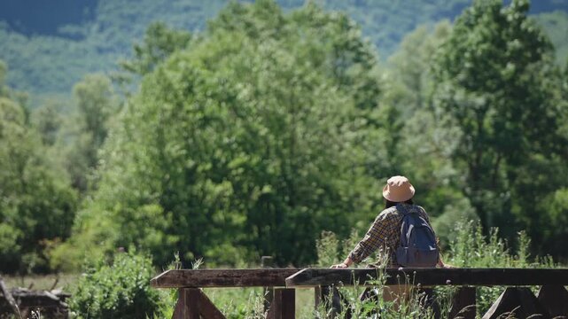 Female traveler with a backpack walking across a scenic bridge over a mountain river surrounded by breathtaking mountain scenery, capturing hiking, adventure and exploration in nature.