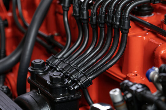 Close-up of black fuel lines connected to a powerful orange engine block. Industrial engineering and mechanical technology concept for heavy machinery.