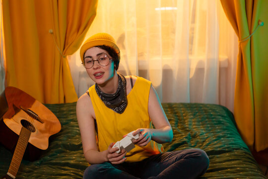 Teenage girl in yellow clothes is immersed in gaming while sitting comfortably on a bed. Concept of home-based entertainment and comfort. Mid shot