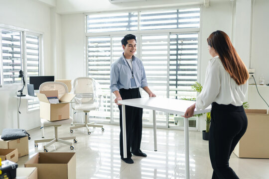 Young asian business coworkers carrying office table together while moving furniture and setting up a new workplace