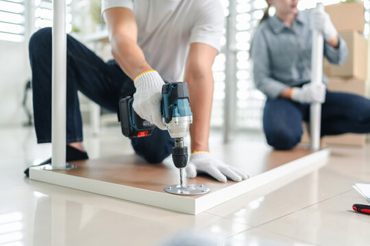Young asian coworkers assembling office furniture together with power drill and hand tools during workplace relocation
