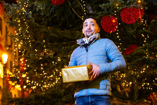 Man receiving holiday gift under twinkling christmas tree lights at night
