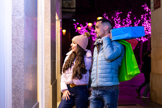 Couple shopping during christmas, admiring store window displays at night