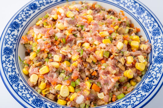 A bowl of pork dumpling filling with corn, vegetables, and mushrooms.