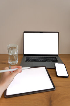 Person using a stylus on a tablet with mockups of laptop and smartphone on a wooden desk, representing digital work, technology and modern productivity