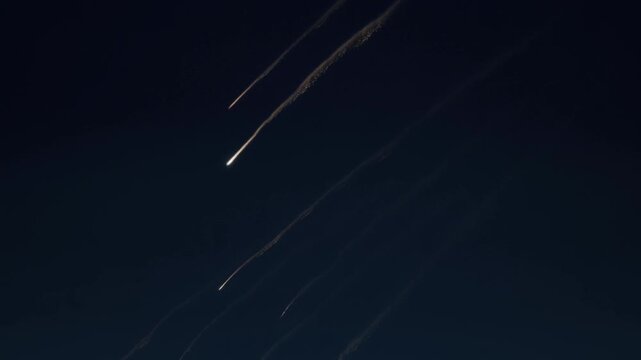 Meteor streaks crossing dark night sky in parallel paths with glowing trails