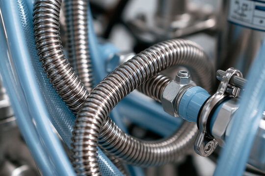 Industrial stainless steel flexible hoses and blue tubes are connected in a machine. This detail depicts mechanical engineering or pharmaceutical processing technology.