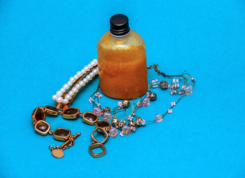 Gold sparkling body gel in bottle surrounded by fashionable shiny jewellery on blue background 