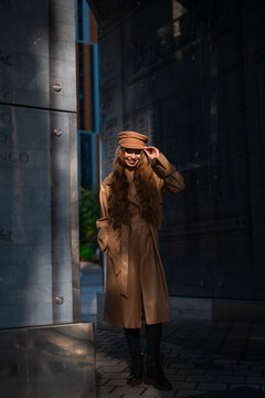 woman posing urban street side view coat hat boots wall inscriptions casual fashion brown black fabric leather concrete light clean background copy space editorial natural vivid modern web.