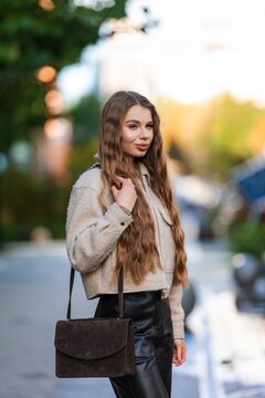 confident woman in stylish jacket and leather pants posing outdoors in urban setting with beige and black tones, frontal view, fashion and street style context.