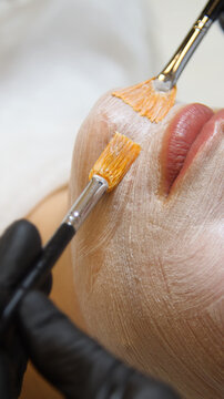 Professional beautician applying cleansing mask on female client's face. Mesotherapy. Close-up of female face during youth restoration and facial rejuvenation procedure.