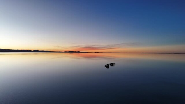 Breathtaking sunset footage over the flooded Salar de Uyuni in Bolivia, featuring a warm golden mirror reflection.