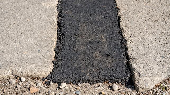 A fresh black asphalt patch contrasts with older gray pavement on a repaired street, bright even daylight, clean overhead composition and clear temporary maintenance result, pothole repair,