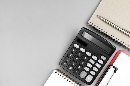 Top view of black calculator with notebooks and pen on gray background with copy space. Concept of accounting, financial planning, budget management, and tax calculation.