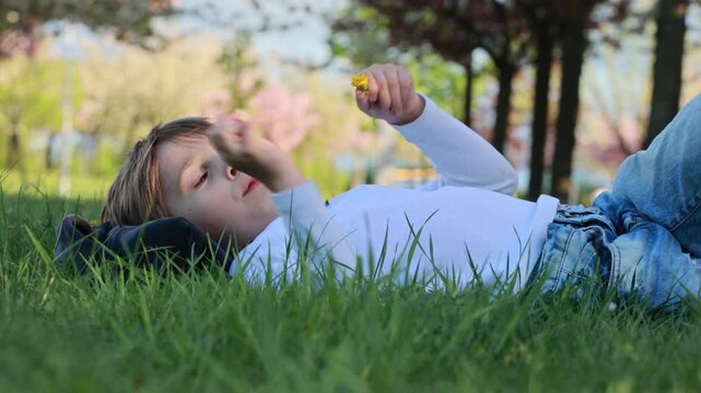 Portrait of cute stylish smiling toddler boy sitting in the grass in park