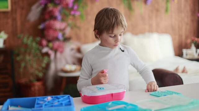 Child, boy, playing with colorful dots, aquabeads, making different figures from small plastic dots