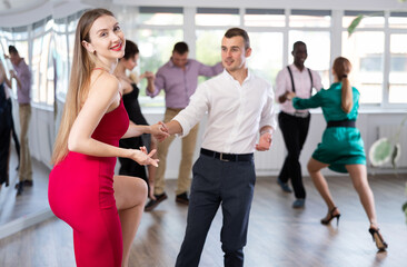 Fototapeta premium Group of happy men and women in festive clothes dancing foxtrot in dance studio