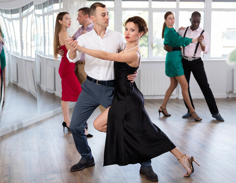 Active young man training waltz in pair with woman in dance-hall during dancing classes