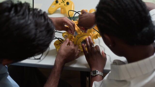 Multiethnic young adults assembling yellow robot kit during STEM workshop, high angle shot. Footage is ideal for educational marketing, engineering courses, and technology training promos
