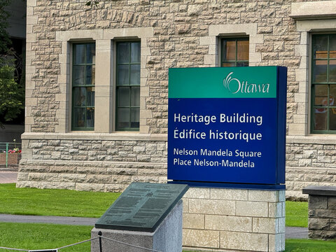 Ottawa, Ontario, Canada. August 24, 2026. Medium shot of the Heritage Building sign at Nelson Mandela Square outside Ottawa City Hall.