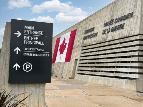 Ottawa, Ontario, Canada. August 25, 2026. Low angle view of the Canadian War Museum entrance sign and concrete building with a Canadian flag.