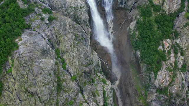 Shdugra Waterfall rushes in aerial view beside a massive cliff wall below Ushba glaciers near Mazeri, Svaneti, supporting trekking tourism, erosion studies, alpine hydrology and Georgian nature media.