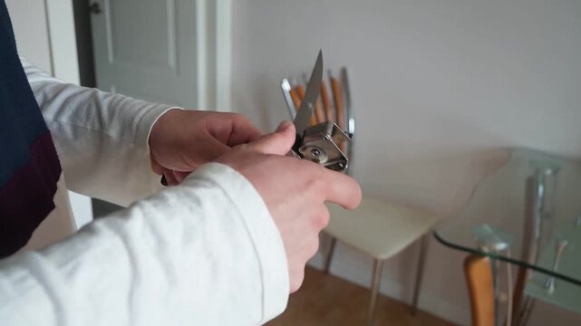 Close Up of Man Sharpening Steel Kitchen Knife with a Manual Sharpener Tool at Home