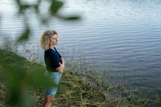 Thoughtful Blonde Mature Woman Standing Alone by Quiet Lake in Peaceful Nature