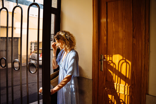 Thoughtful Mature Blonde Woman Leaving Home with Straw Bag in Warm Morning Sunlight