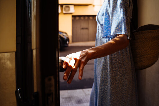 Close Up of Mature Woman Hand Opening Front Door While Leaving Home with Straw Bag