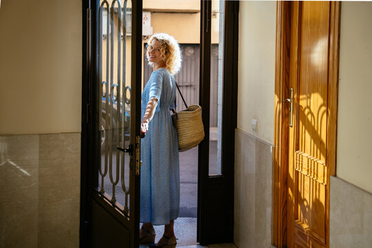 Full Length Smiling Mature Blonde Woman Leaving Home with Straw Bag on Sunny Summer Morning