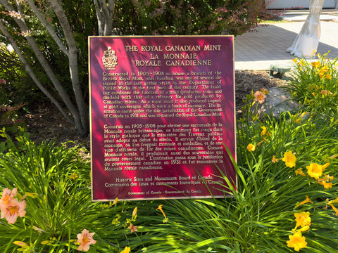 Ottawa, Ontario, Canada. August 25, 2026. Medium shot of a historical plaque for The Royal Canadian Mint placed in a garden with yellow flowers.