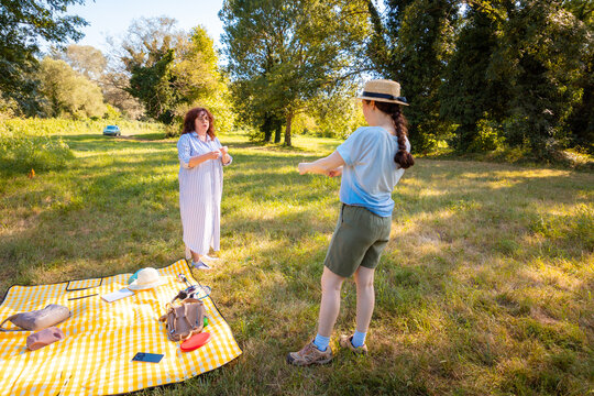 A grown daughter and her mother relax together on a picnic blanket in a summer park enjoying healthy leisure and family time in a serene green setting. Full length shot