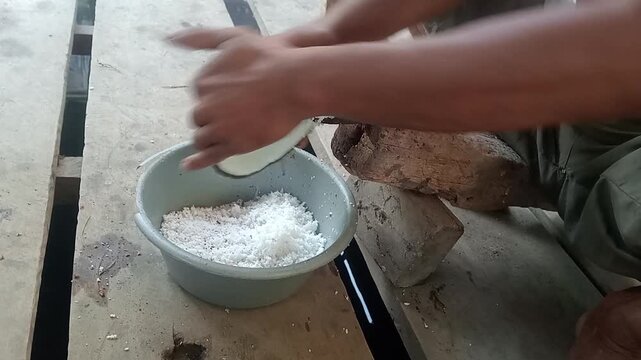 Farmer grating fresh coconut meat using traditional manual tool into a bowl