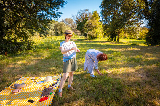 Caucasian mother and grown daughter share a joyful summer picnic in a bright park connecting over food, conversation, and family leisure outdoors. Wide shot