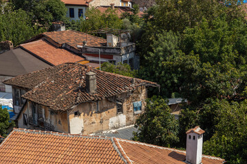 Fototapeta premium Old dilapidated historic houses with weathered tiled roofs and rustic walls hidden in greenery in Kaleici old town of Antalya, Turkey. Heritage architecture view.