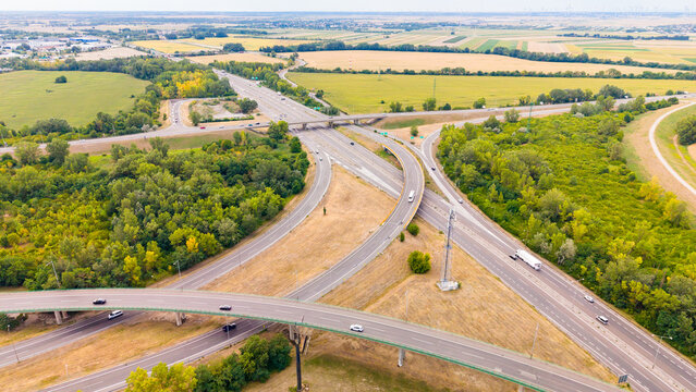 Highway junction surrounded by fields and greenery near a city. Vehicles travel along a busy highway junction with fields and trees nearby.
