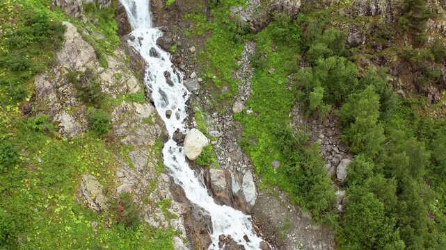 Glacial stream descends in landing aerial view through boulders and alpine vegetation below Shdugra Waterfall, supporting hydrology study, trekking routes, erosion monitoring and Svaneti travel media.