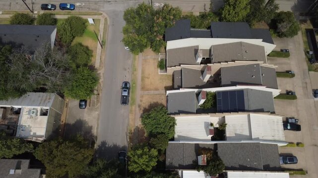 Stepped residential rooflines border Welborn Street alleyways in Dallas. Photovoltaic solar arrays, brick chimneys, parked vehicles flank narrow paved neighborhood driveways, Texas