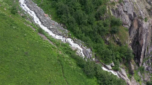Glacial stream descends in landing aerial view along a green alpine slope near Mazeri, Svaneti, supporting watershed monitoring, trekking tourism, mountain ecology and Georgian destination media.