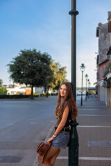 Fototapeta premium Young Woman Posing by Streetlamp with Cowboy Hat. Young woman with long brown hair posing beside a streetlamp in denim shorts and a brown top while holding a cowboy hat.