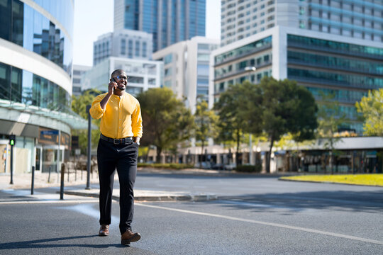African american smiling businessman talking on phone call, business communication, walking, near glass office building. Mid age Black man works as Leader, checking weather app, tech savvy lifestyle.