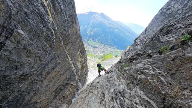 Climber ascending steep vertical rock face inside a narrow passage on Dauberhorn Via Ferrata, Switzerland
