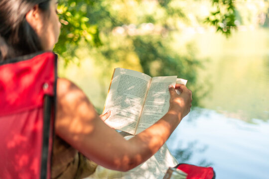 Woman reading book outdoors by lake relaxing