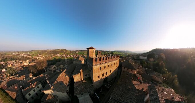 Drone flying over Medieval Castell'Arquato fortress towers and historic village rooftops at sunset in Italy. Aerial forward, copy space
